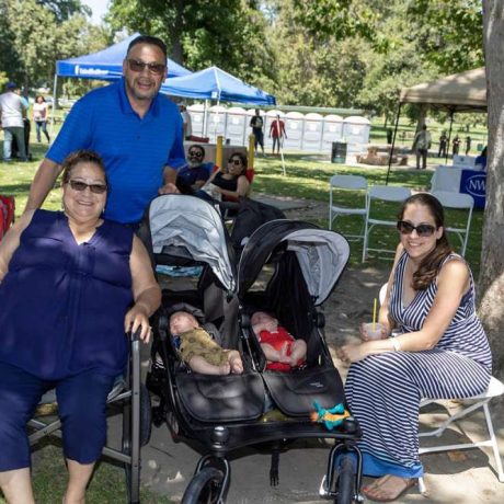 group of people smiling together for photo on a sunny day with babies in stroller