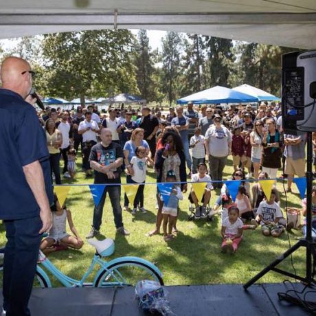 man using microphone speaking to large crowd at park