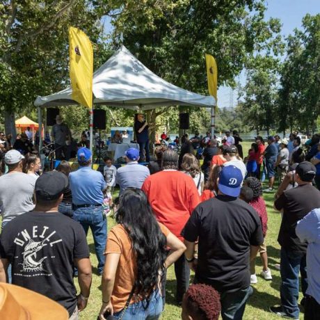 large crowd at park listening to man speaking over mic