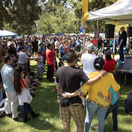 man speaking on microphone to large crowd at a park