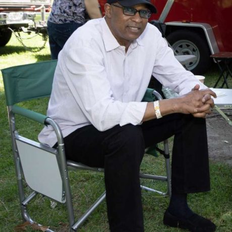 man smiling at camera sitting on a folding chair in a grassy area