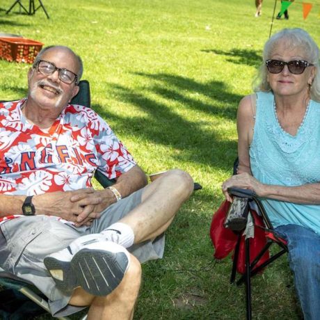 two people smiling for photo sitting on folding chairs in grassy area