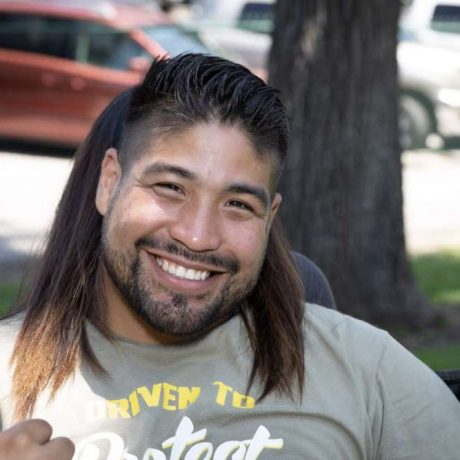 man smiling and giving thumbs-up with another person leaning on him