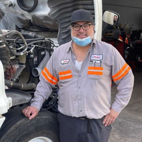 man smiling in front of truck with engine exposed for maintenance