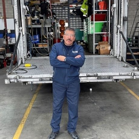 man standing in front of truck in work clothing posing for photo