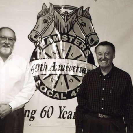 karl ullman smiling in front of teamsters 495 60th anniversary poster with friend